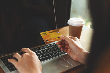 Close-up of a woman holding a credit card while using a laptop on a wooden table with a coffee cup...