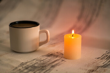 Cozy scene with candle and coffee mug. This scene evokes a sense of comfort and relaxation. Use for themes related to home and cozy atmospheres. Selective focus.