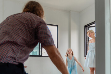 Obraz premium Candid moment of a family playing joyfully in the empty, spacious room of their new house. Daughter running towards her father in a game of hide and seek after moving into a new home.