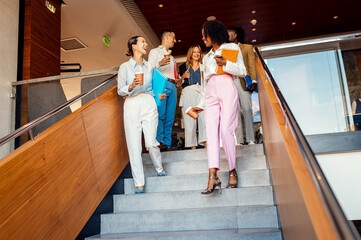 Group of diverse colleagues walking down stairs in office, discussing work in modern business space.