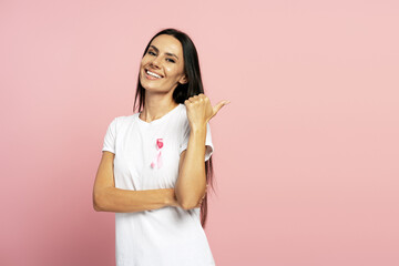 Woman pointing aside while showing pink ribbon for breast cancer awareness