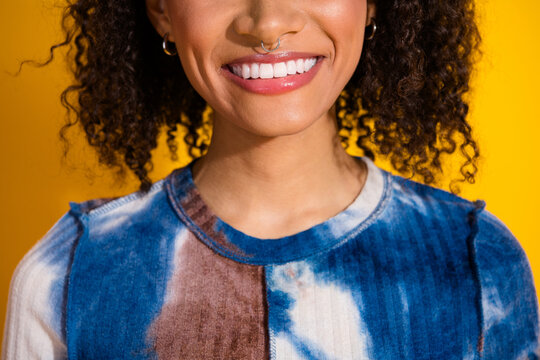 Young woman with curly hair smiling confidently against vibrant yellow background wearing a fashionable tie-dye top