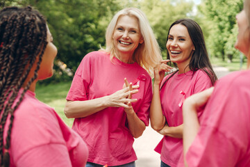 Women wearing pink ribbons supporting breast cancer awareness month talking together in a park