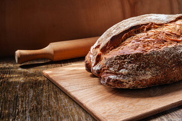Freshly baked rustic bread on a wooden board with a rolling pin in a cozy kitchen setting