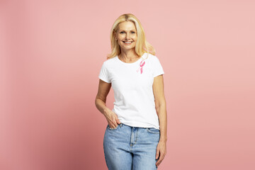 Smiling woman wearing pink ribbon for breast cancer awareness posing on pink background