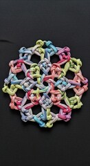 A colorful, intricate, hand-crafted, geometric knot design on a dark surface.