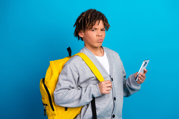 Portrait of a stylish teenage boy with a phone and a yellow backpack in front of a bright blue background