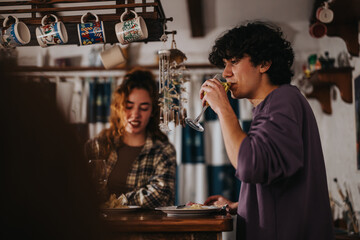 A casual scene of two young friends indoors, conversing and sipping beverages by a bar. The ambient...
