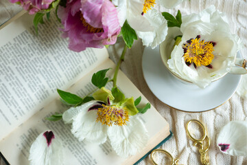 Peony flowers and a cup of tea, books on a white blanket.