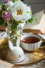 Peony flowers and a cup of tea, books on a white blanket.