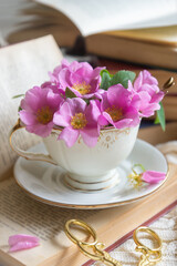 A cup of aromatic tea, a book and a rose on the table.