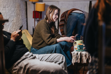A group of friends spending time together in a warm and cozy environment, each engaged with mobile devices, creating a modern and casual ambiance. The image highlights connection and relaxation.