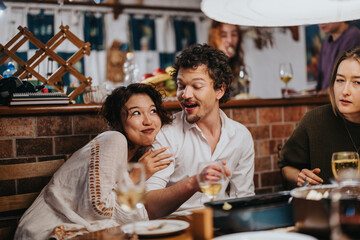 A group of friends interact at a cozy indoor setting. They are sharing food, conversation, and laughter, creating a warm social atmosphere around the table in a lively and friendly environment.
