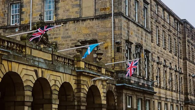 Scottish and British flags hanging on historic stone building in Edinburgh. National symbols fluttering on facade of old architecture in Scottish capital. Flags waving on government structure in