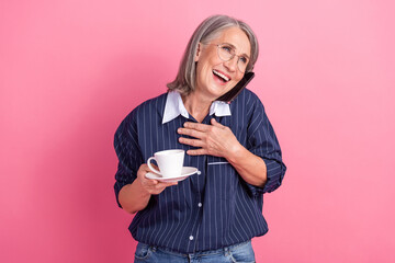 Happy senior businesswoman multitasking with coffee and phone against a pink background
