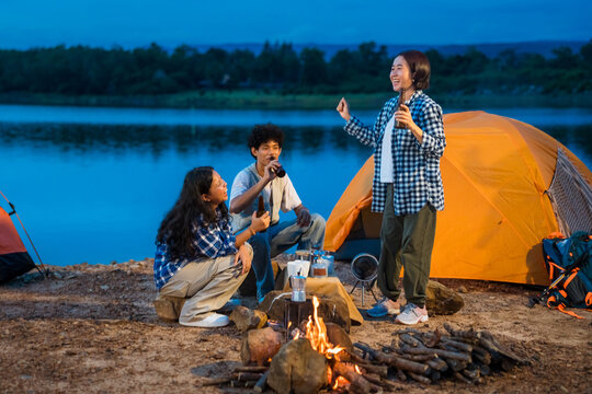Three people are sitting around a campfire. Group of friends enjoy outdoor camping, a celebration of friendship, connection, and togetherness around a campfire. - Powered by Adobe