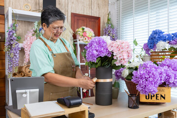 Asian senior woman, florist, small business owner, entrepreneur arranges flowers with passion at shop, showing creative occupation, independent lifestyle, customer service, retirement, aging society