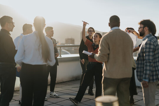 A group of multiracial, business colleagues gather on a rooftop terrace to celebrate success with music and dance during sunset. The mood is joyous and relaxed, showcasing teamwork and camaraderie.