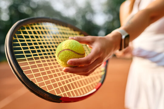 Female hand holding tennis ball on racket during outdoor game on clay court in summer