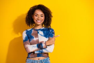 Confident young woman pointing and smiling against vibrant yellow background, showcasing casual...