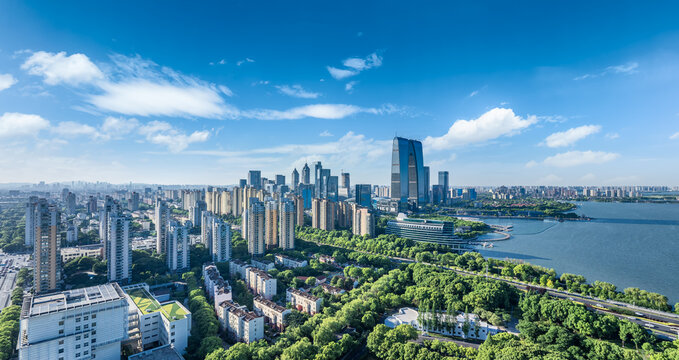 Modern city commercial buildings with green park and a large lake under a bright blue sky in Suzhou, China.