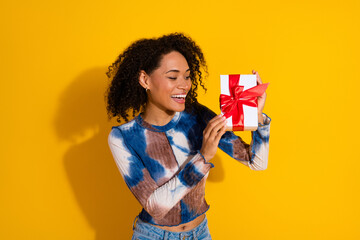 Excited young woman holding a gift box with a red ribbon against a vibrant yellow background