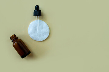 Flat lay bottle with a pipette and a cotton pad on a beige background.