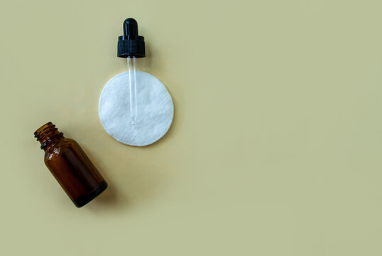 Flat lay bottle with a pipette and a cotton pad on a beige background.