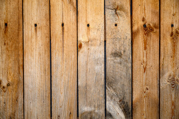 The vertical wooden planks are placed closely together, highlighting their natural grain and warm tones. The wood has a rustic look, with various knots and imperfections for copy space.