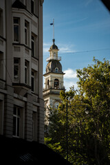 An ornate clock tower with a domed top and balcony rises behind classic stone buildings and leafy...