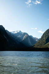 Sunlight cuts across rugged, forested mountains surrounding a tranquil lake, revealing a...