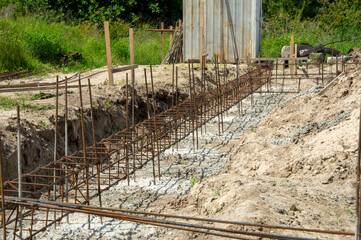 Workers prepare a foundation at a construction site, laying rebar in a trench for structural...