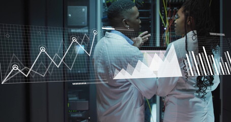 Gesturing engineers in lab coats reviewing metrics on laptop in data center, with racks and cables