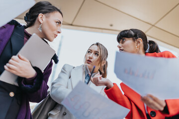 Three businesswomen discussing charts outdoors during a collaborative work meeting.