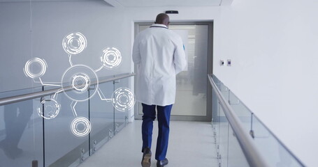 Walking doctor wearing lab coat down hospital hallway, with glass railing, digital network overlay