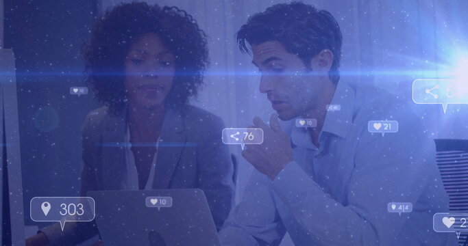 Collaborating colleagues reviewing social media metrics at office, with laptop and floating icons
