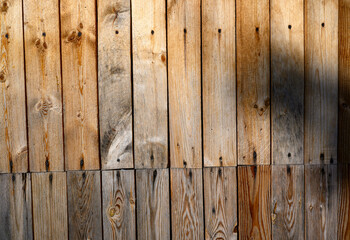 Vertical wooden planks create a rustic and natural appearance,with varying shades of brown and visible grain patterns.Shadow partially casts over the surface, adding depth and contrast,for copy space.