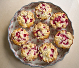 Overhead shot of berry muffins in a round floral dish on rustic wooden table, cozy and homebaked flatlay scene.
