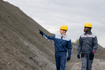 Surveying engineers at sand quarry, caucasian and african adult males in ore mining open mine