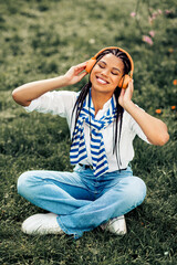 Cute woman with braids enjoying music in the park on a sunny spring day, seated in a casual outfit...