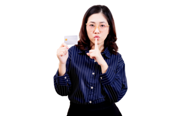 Asian young beautiful woman with glasses holds a card and gestures shushing with her finger to her lips.