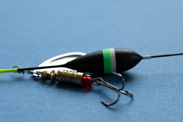 Fishing tackle including a float and a lure on a blue background. The float is black with a green...