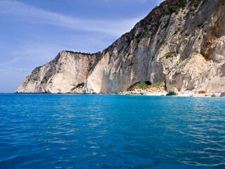 Fototapeta premium Mizithres Beach on Zakynthos Island viewed from the sea, featuring cliffs, turquoise water and clear blue sky in sunlight.