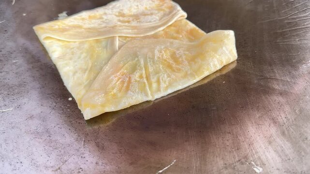 4k Street food vendor is preparing the dough and pan-frying paratha roti in hot oil until crispy on the outside. Street hawker preparing prata bread or roti canai for morning 