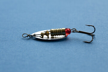 A shiny fishing lure with a red bead and treble hook on a blue background. 