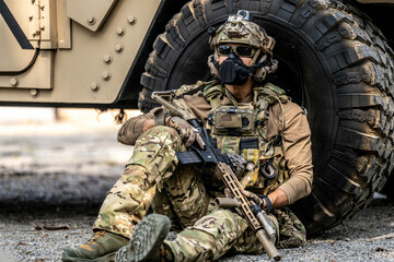 Special Forces Soldier Resting Under Armored Vehicle – Tactical Gear, Rifle Ready, Combat...