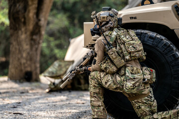 Special Forces Soldier Resting Under Armored Vehicle – Tactical Gear, Rifle Ready, Combat...