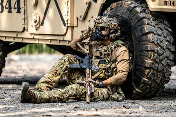 Special Forces Soldier Resting Under Armored Vehicle – Tactical Gear, Rifle Ready, Combat...