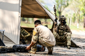 Special forces soldiers preparing tactical gear at military field base camp with weapons and...
