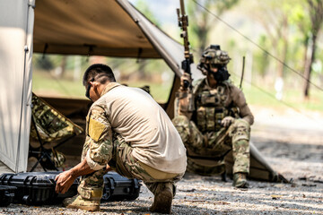 Special forces soldiers preparing tactical gear at military field base camp with weapons and...